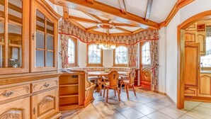 A spacious kitchen with wooden cabinetry, a dining area with a round table and chairs, and large windows with curtains. - Spacious flat in Adenau near the Nürburgring (Adenau)