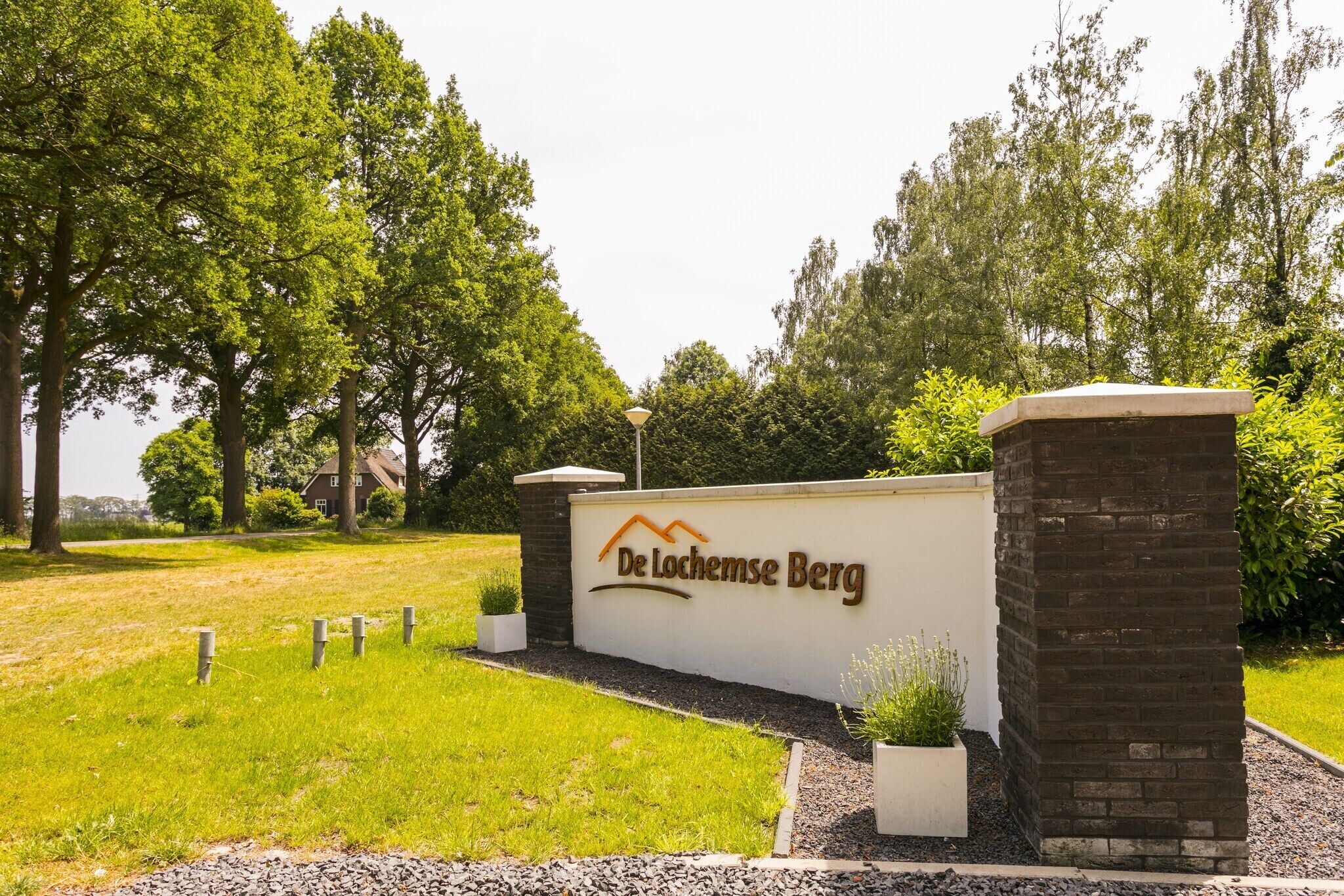 A sign for De Lochemse Berg with a landscaped entrance and a brick wall.