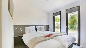 Une chambre moderne avec un grand lit, une tête de lit, une table de chevet et une vue sur l’extérieur grâce à une porte coulissante.
