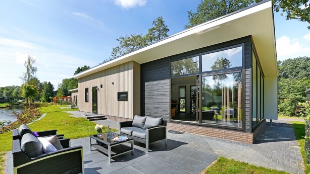 Une maison moderne dotée d’un patio aménagé avec du mobilier d’extérieur et offrant une vue sur un lac.