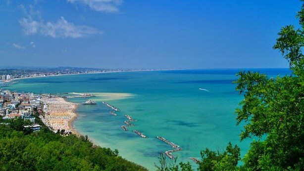 Un paisaje costero con playa, aguas azules cristalinas y un horizonte urbano distante.