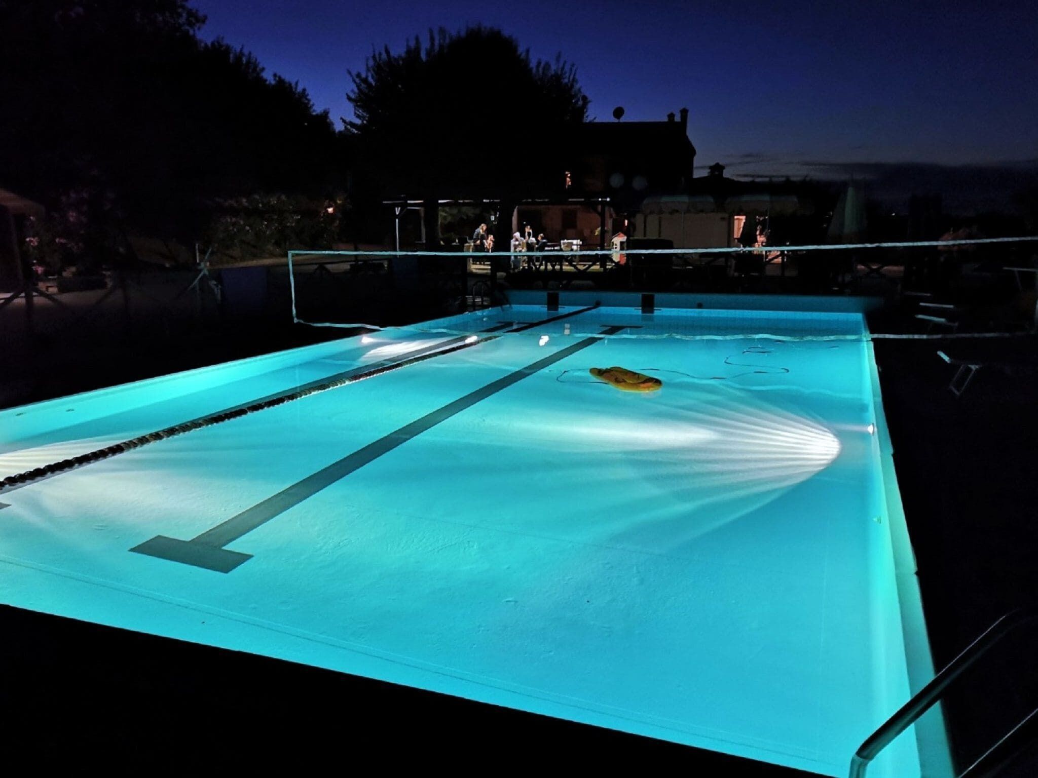An outdoor swimming pool at dusk with lane dividers and a lifeguard stand in the background.