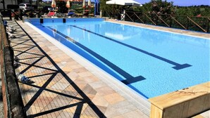 Una piscina con cubierta de baldosas, sillas de descanso y sombrillas.