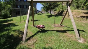 Un ensemble de balançoires en bois installé dans un espace herbeux, avec un bâtiment en pierre en arrière-plan.
