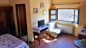 Une chambre avec un lit, un bureau avec un ordinateur, un radiateur et une fenêtre donnant sur des arbres.