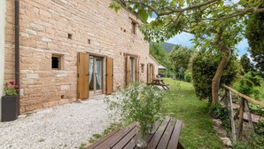 A stone building with wooden shutters, a gravel pathway, and a wooden bench.