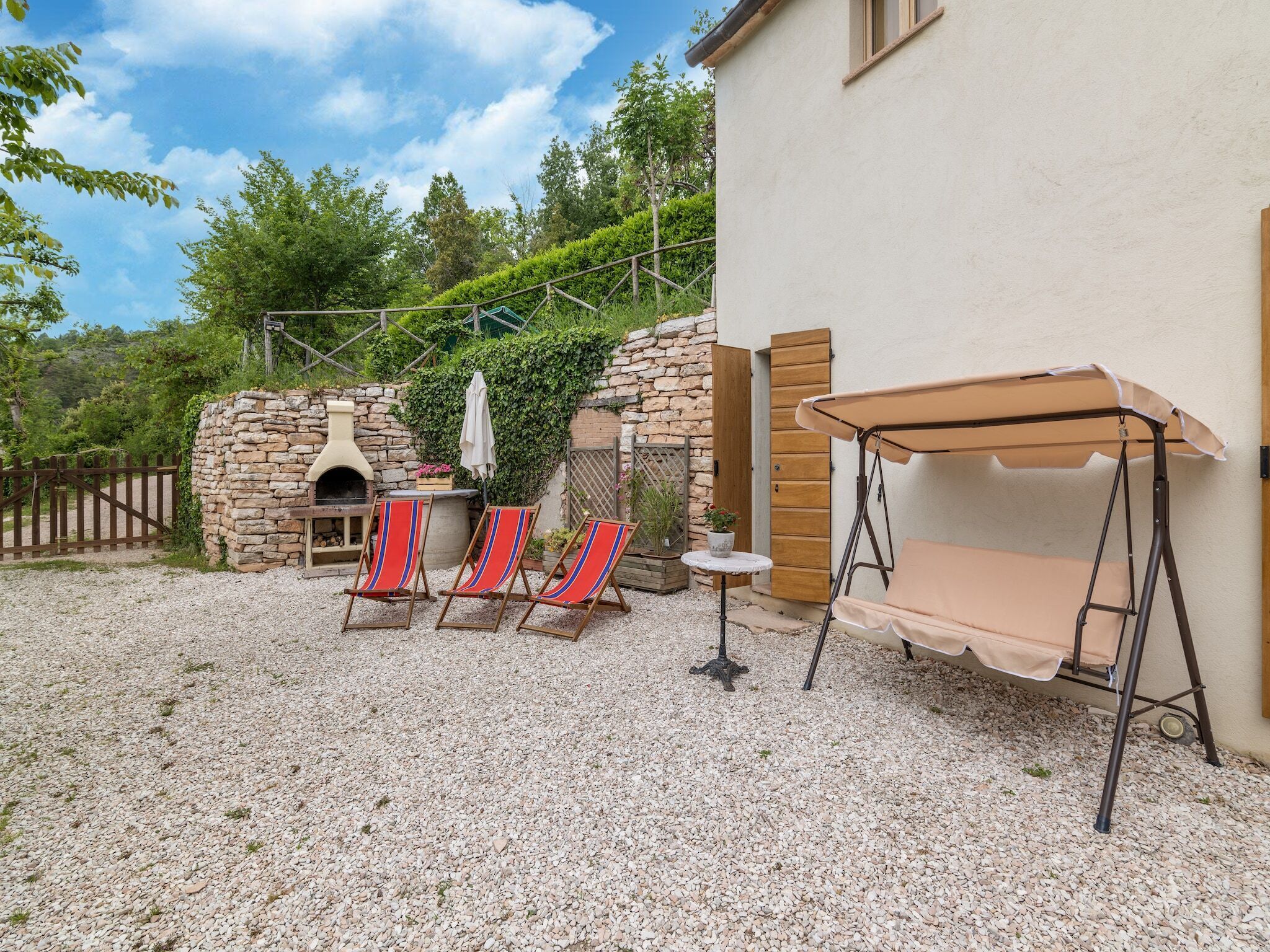 A patio with a stone wall, a barbecue grill, and three red and blue striped lounge chairs.