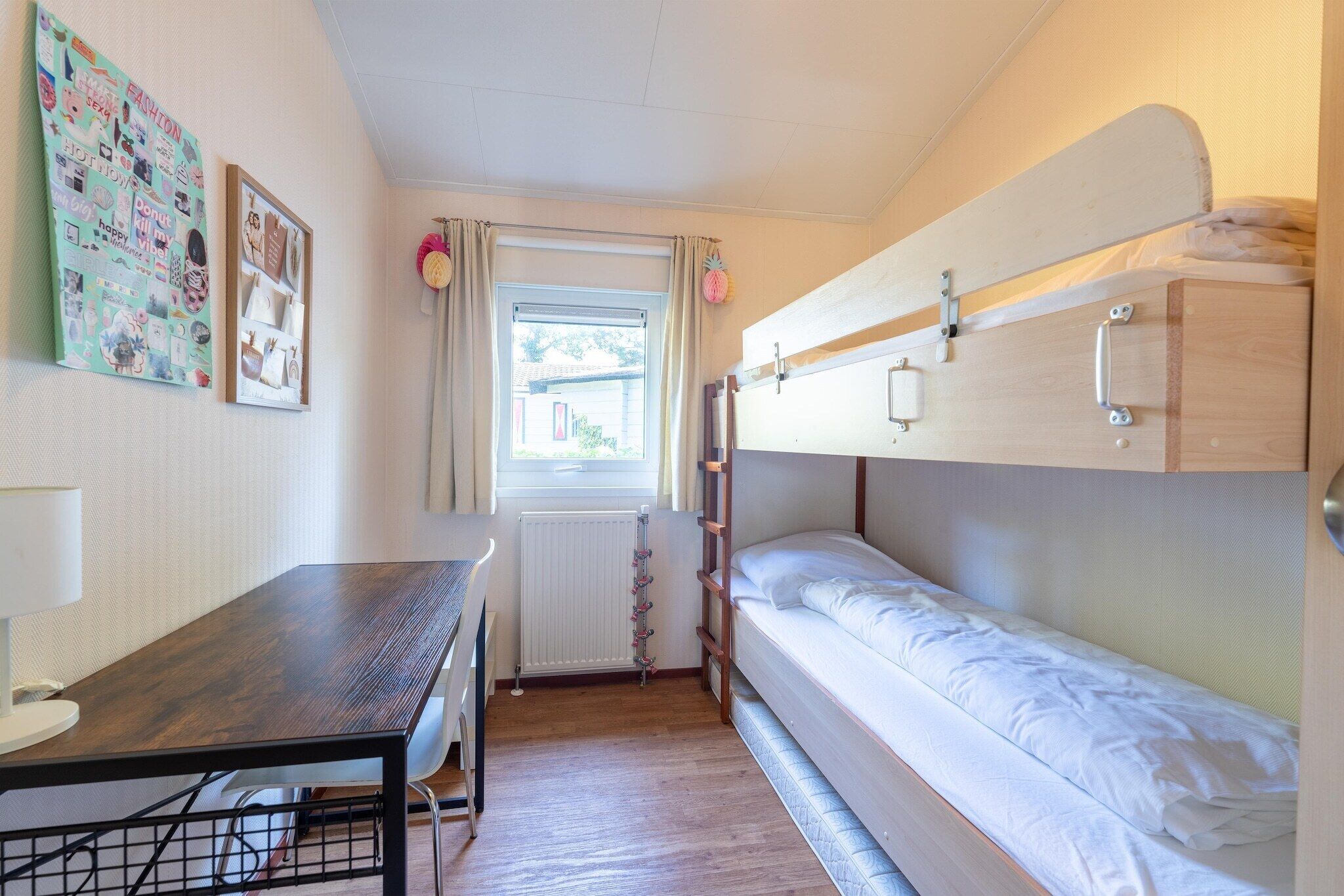 Een kleine kamer met stapelbedden, een bureau en een raam met gordijnen.