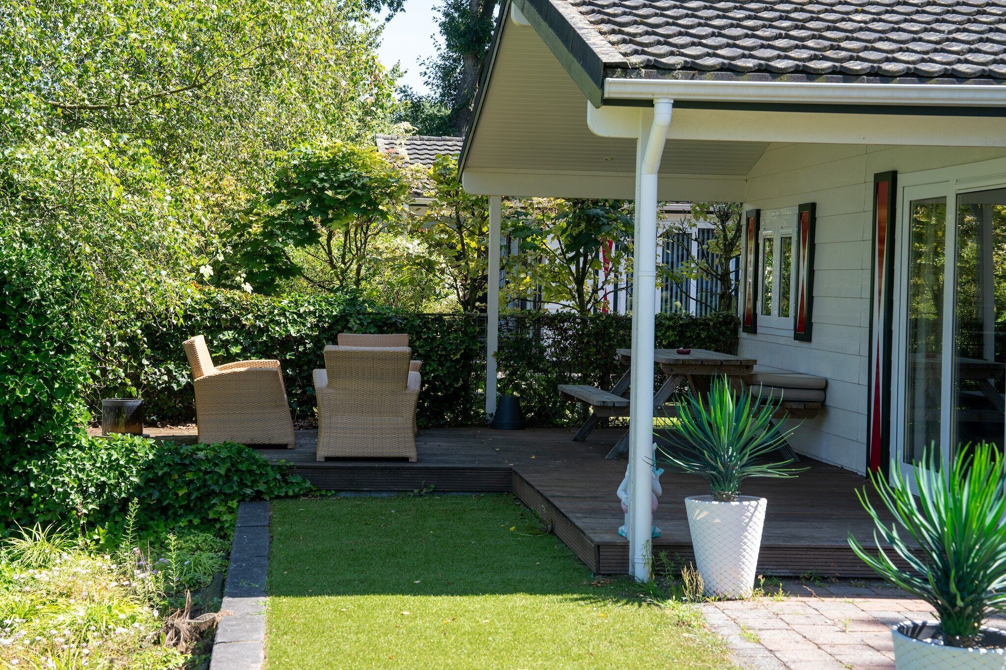 Een overdekt terras met rieten meubels, een tafeltje en plantenpotten.