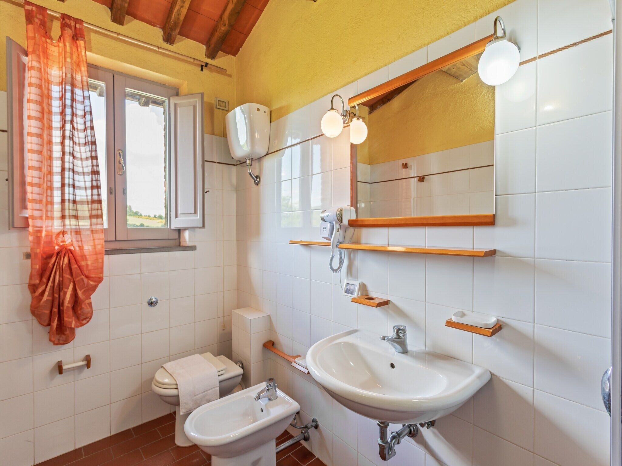 A bathroom with a toilet, bidet, sink, and a window with a curtain.