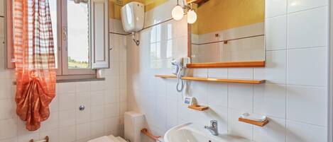A bathroom with a toilet, bidet, sink, and a window with a curtain.
