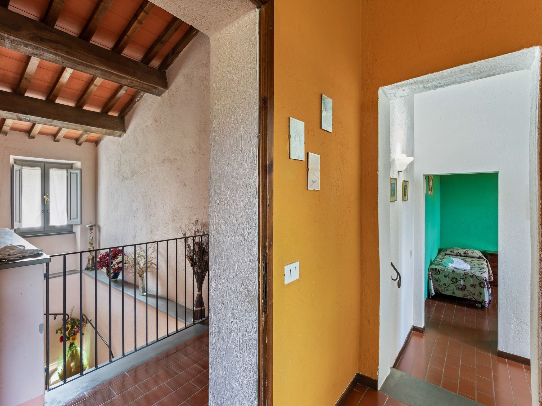 A room with a wooden ceiling, a balcony with a railing, a window with shutters, and a bed with a floral bedspread.