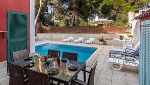 Un área de piscina con sillones reclinables, una mesa de comedor con sillas y una pequeña mesa con una planta en maceta.