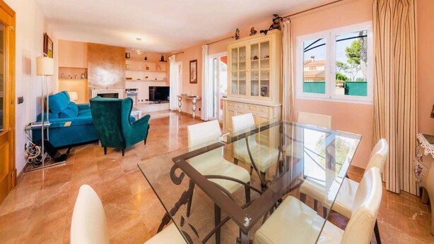 Un amplio espacio de sala con una mesa de vidrio, un sofá color turquesa y una cocina al fondo.