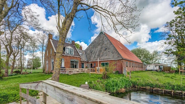 Une maison traditionnelle néerlandaise avec un toit rouge, une terrasse en bois et un étang au premier plan.