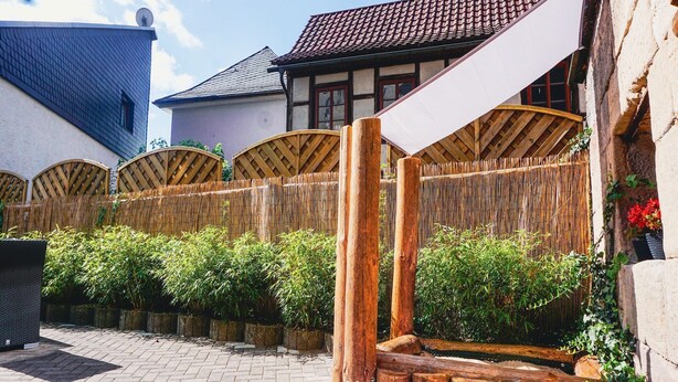 Une cour entourée d’une clôture en bois, avec un chemin en briques et un bâtiment traditionnel doté d’un toit en tuiles.