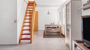 Un intérieur moderne avec un escalier en bois, un coin repas et un téléviseur posé sur un meuble en bois.