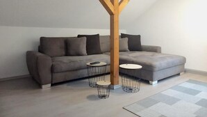 Un salon moderne avec un canapé gris, deux petites tables rondes et une structure de plafond en bois.