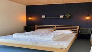 Cama bem arrumada com estrutura de madeira e roupa de cama branca, em quarto com paredes escuras e carpete azul.