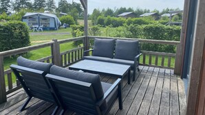 Um deck externo com piso de madeira, duas cadeiras cinzas estofadas e uma pequena mesa.