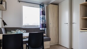 A compact kitchen with a dining area, a built-in wooden cabinet, and a window with a curtain. - Chalet in Nature, Friesland (De Veenhoop)