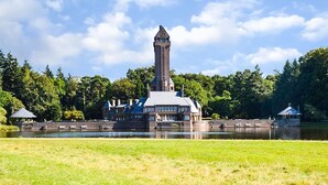 Ein großes Gebäude mit einem markanten Turm, umgeben von Wasser und üppiger Vegetation.