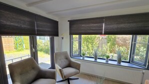 Ein modernes Wohnzimmer mit zwei Sesseln, einem runden Couchtisch und großen Fenstern mit dunklen Jalousien.