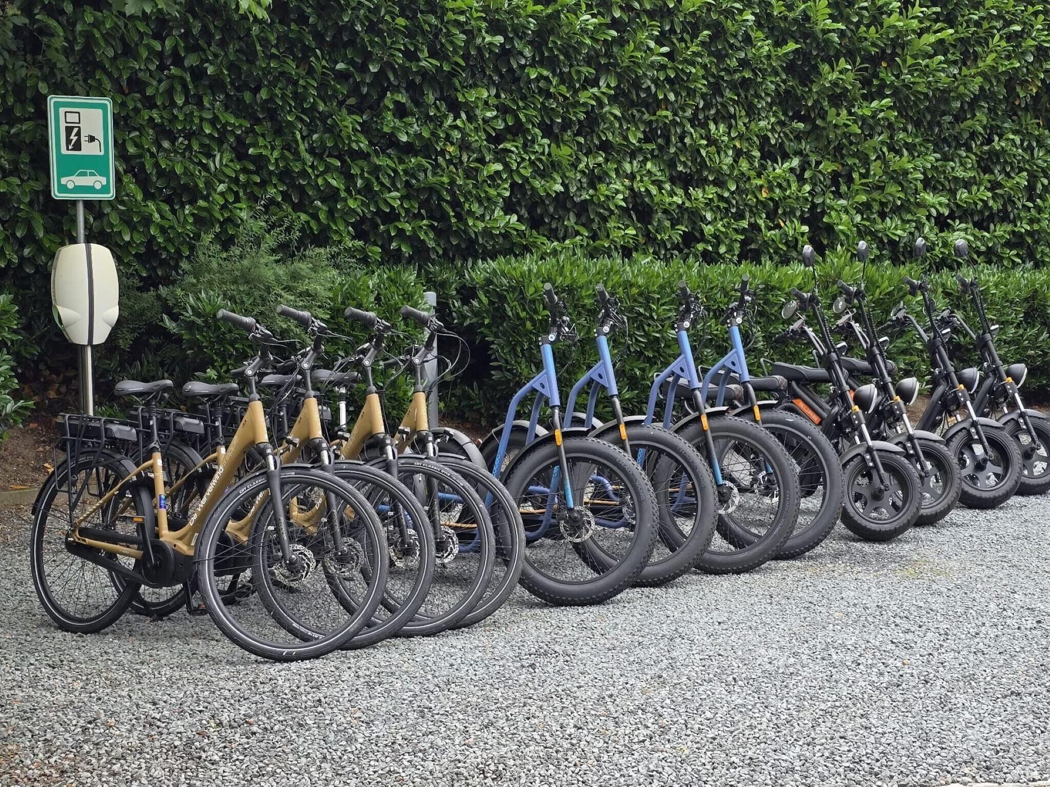 Varias bicicletas estacionadas sobre grava, con un cartel verde que indica zona de estacionamiento.