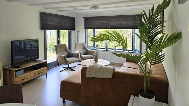 Ein modernes Wohnzimmer mit Flachbildfernseher, Ledersofas und großen Fenstern mit Jalousien.