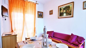 A dining area with a table set for four, a sofa, and a painting on the wall. - Apartment in Rosolina Mare near the Sea (Rosolina Mare (RO))