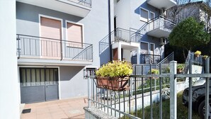 A residential building with a gated entrance, a balcony with a flower pot, and a visible door number. - Apartment in Rosolina Mare near the Sea (Rosolina Mare (RO))