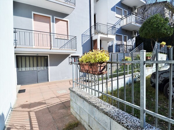Un immeuble résidentiel doté d’une entrée sécurisée par un portail, d’un balcon agrémenté d’un pot de fleurs et d’un numéro de porte bien visible.