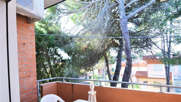 A balcony with a white table and chairs, a lantern, and a view of trees and buildings. - Apartment in Rosolina Mare near the Sea (Rosolina Mare (RO))