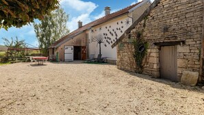 A rustic stone building with a gravel courtyard, a wooden door, and a tree mural on the wall.