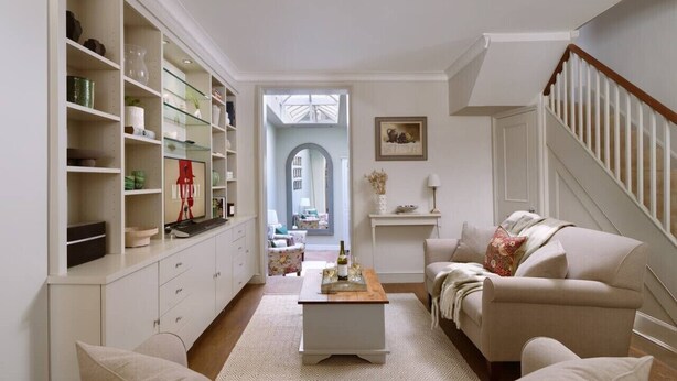 A living room with a sofa, coffee table, and shelves. There is a staircase to the right and a door leading to another room. - Kings Road, Chelsea, sleeps 6 (London)