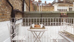 A small outdoor patio with two white metal chairs and a table, a brick wall, and a metal fence. - Kings Road, Chelsea, sleeps 6 (London)