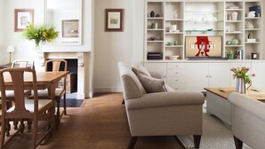 A modern living room with a sofa, a dining table with chairs, a fireplace, and a bookshelf with various items. - Kings Road, Chelsea, sleeps 6 (London)