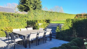Un patio al aire libre con una mesa y sillas, rodeado de setos cuidados y un césped.