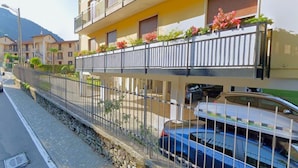 Un edificio residencial de varios pisos con balcones, un muro de piedra de contención y un coche estacionado.
