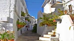 Una calle estrecha con edificios blancos, plantas en macetas y un cielo azul despejado.