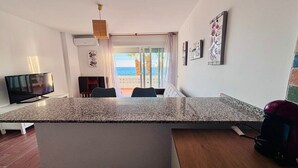 Una cocina moderna con encimera de granito, un comedor con mesa y sillas, y vista al mar a través de una puerta de cristal.