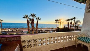 Un balcón con vista al mar, palmeras y coches estacionados.