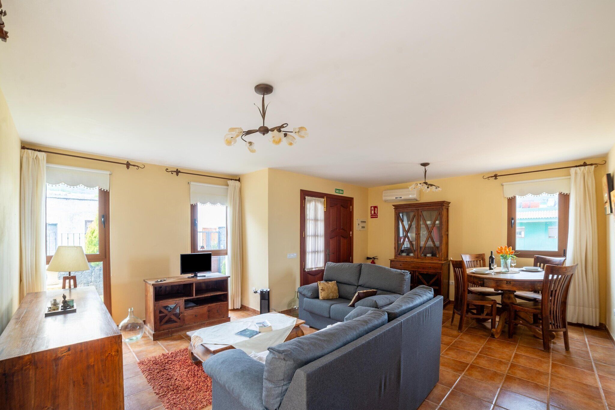 A living room with a sofa, TV, wooden cabinet, and a dining table with chairs.