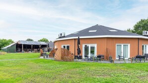 A circular building with a flat roof, large windows, and a covered outdoor seating area with chairs and tables. - Holiday Home in Forested Netherlands with Terrace (Goirle)