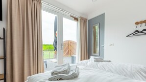 A hotel room with two beds, a sliding glass door to the outside, and a wooden chair visible through the door. - Holiday Home in Forested Netherlands with Terrace (Goirle)
