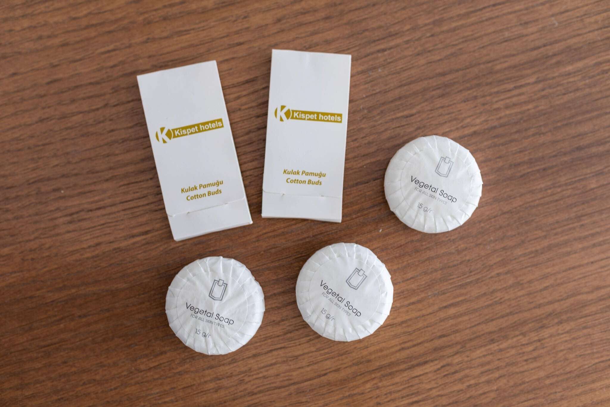 Drei weiße Kartons und zwei runde Seifenpackungen mit dem Aufdruck 'Vegetal Soap' auf einer Holtoberfläche.