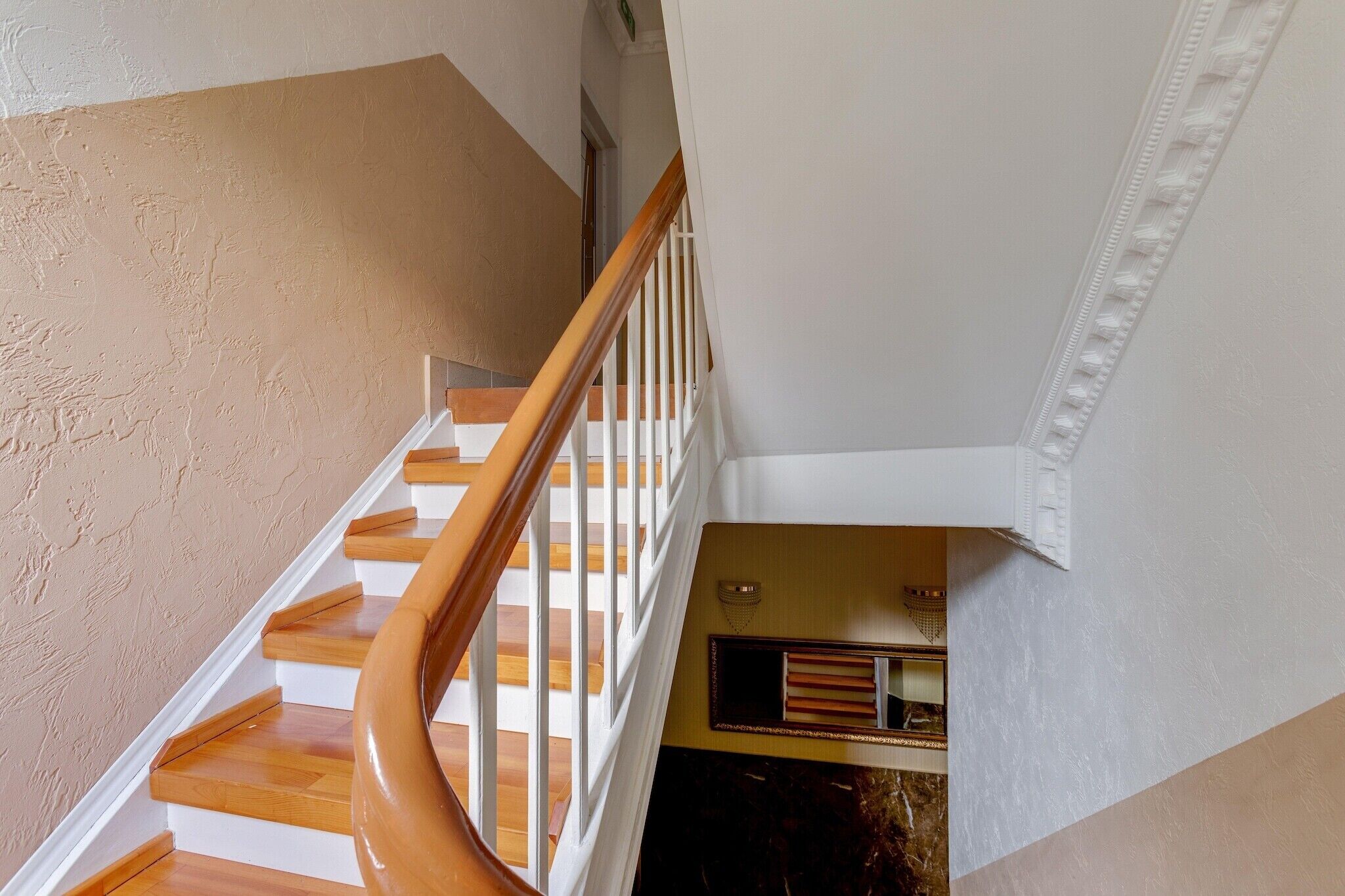 A staircase with wooden steps and white railings, leading to a landing with a small window and a decorative molding.