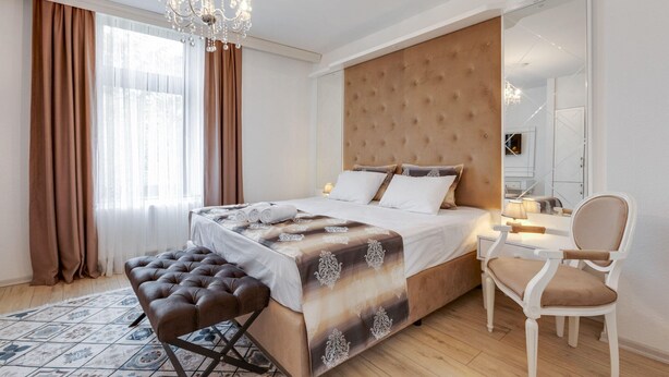A bedroom with a large bed, a bedside table, a chair, and a chandelier.