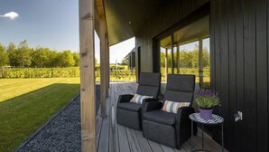 A modern outdoor seating area with two cushioned chairs and a small table, overlooking a grassy field.