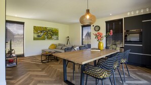 A modern kitchen with a dining area, featuring a wooden table, black chairs, and a hanging light fixture.